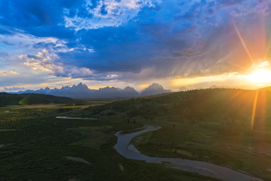 Aerial view of Jackson Hole ranchland at sunset, a winding river through green meadows beneath the Teton range.