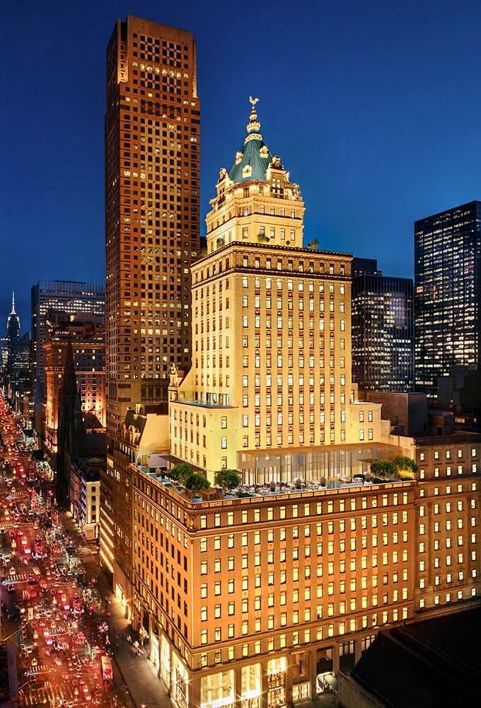 The landmarked King Cole tower rising above Fifth Avenue at blue hour, city traffic streaking below — an icon of long-horizon luxury real estate and hospitality